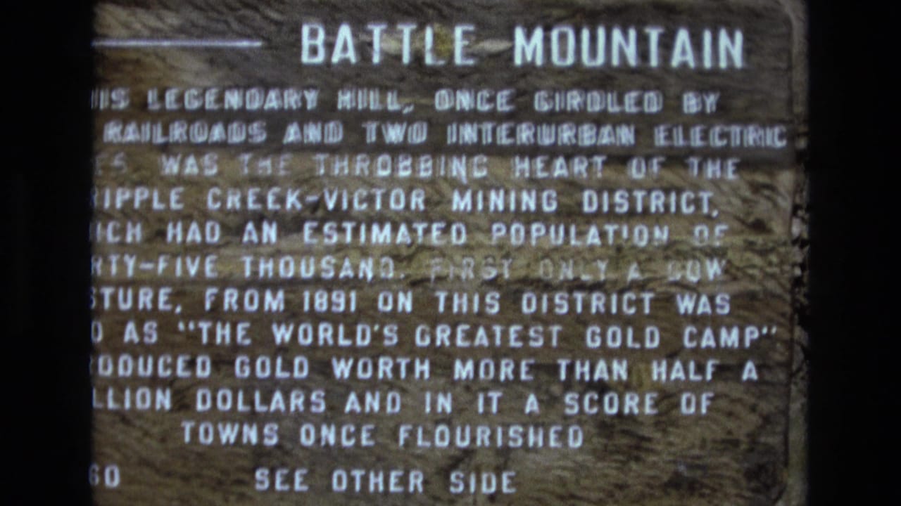 Close 1973 Colorado home-movie view of a weathered wooden Battle Mountain marker with white painted text and a left-pointing arrow.