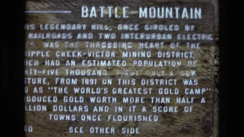 Close 1973 Colorado home-movie view of a weathered wooden Battle Mountain marker with white painted text and a left-pointing arrow.