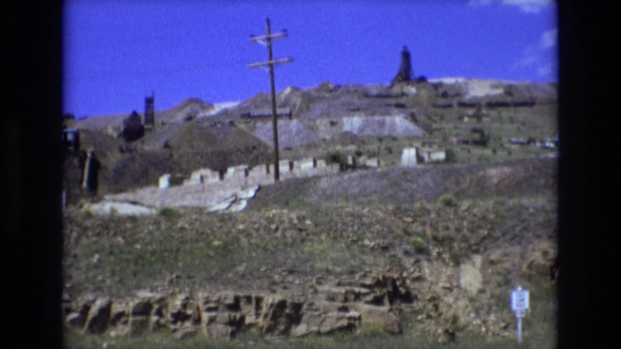 Hillside excavation with utility pole, low buildings, sign, and distant industrial structure.