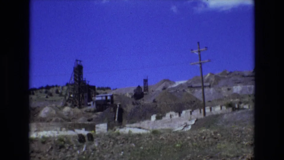1973 Colorado Springs-area home-movie frame with a mine structure, rocky spoil piles, a utility pole, and low mountains in the background.