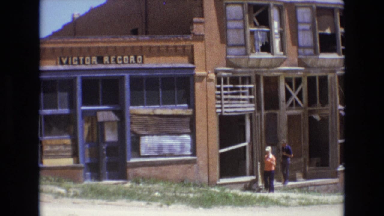 1973 Colorado Springs street view showing two pedestrians near a dilapidated brick storefront with blue trim, broken windows, and a visible Victor Record sign.