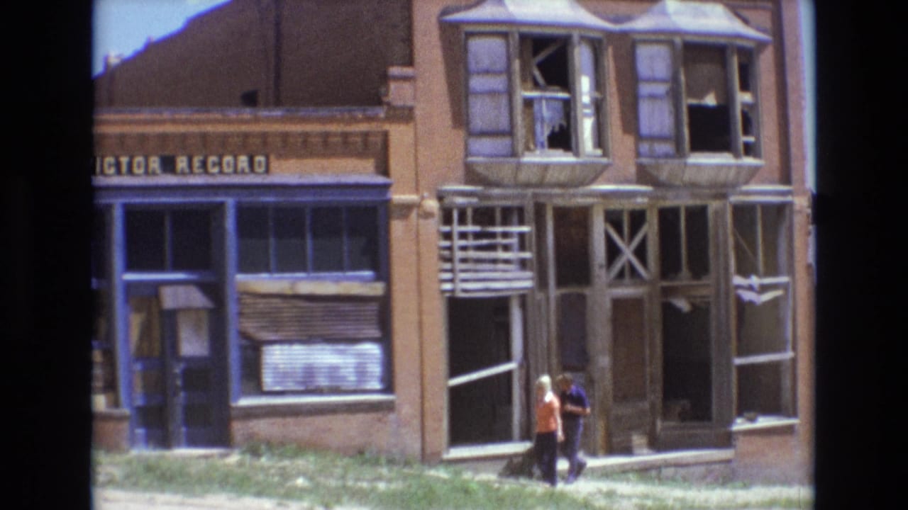 Two pedestrians walk beside a damaged storefront with broken upper windows.
