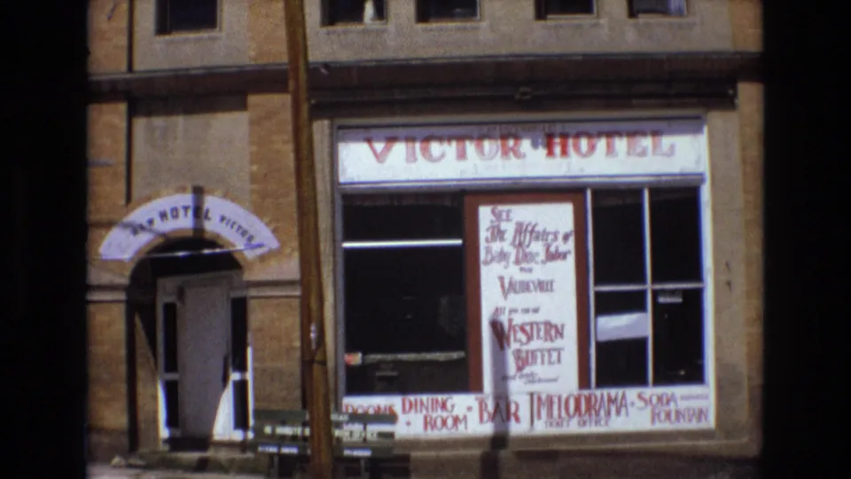 The Victor Hotel exterior in Colorado Springs appears with an open doorway, arched canopy, storefront windows, and prominent 1970s hotel and dining signage.