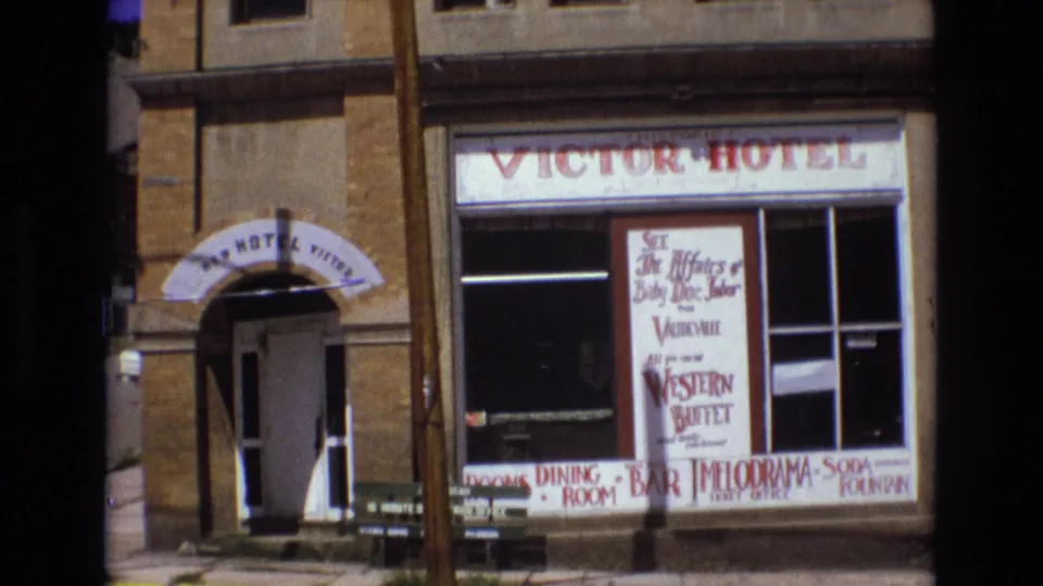 A closer 1973 view of the Victor Hotel street frontage shows the arched entry, storefront glass, large hand-lettered poster, and signs for dining, bar, and buffet service.