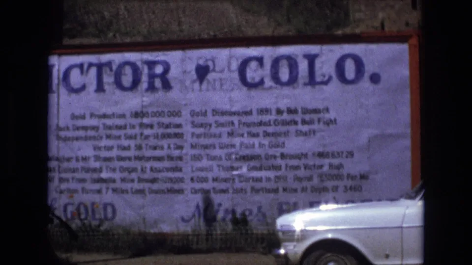 A roadside informational sign for Victor, Colo. dominates the frame, with a white car partially visible at the edge in 1973 Colorado home-movie footage.