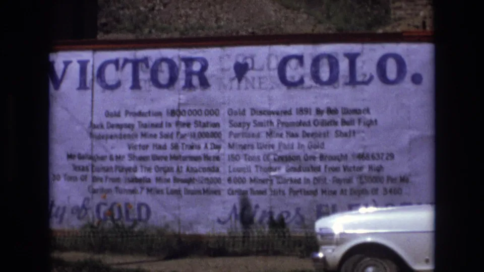 The camera holds on a Victor, Colo. sign with mining-history text while the front of a white car remains visible in the lower right.