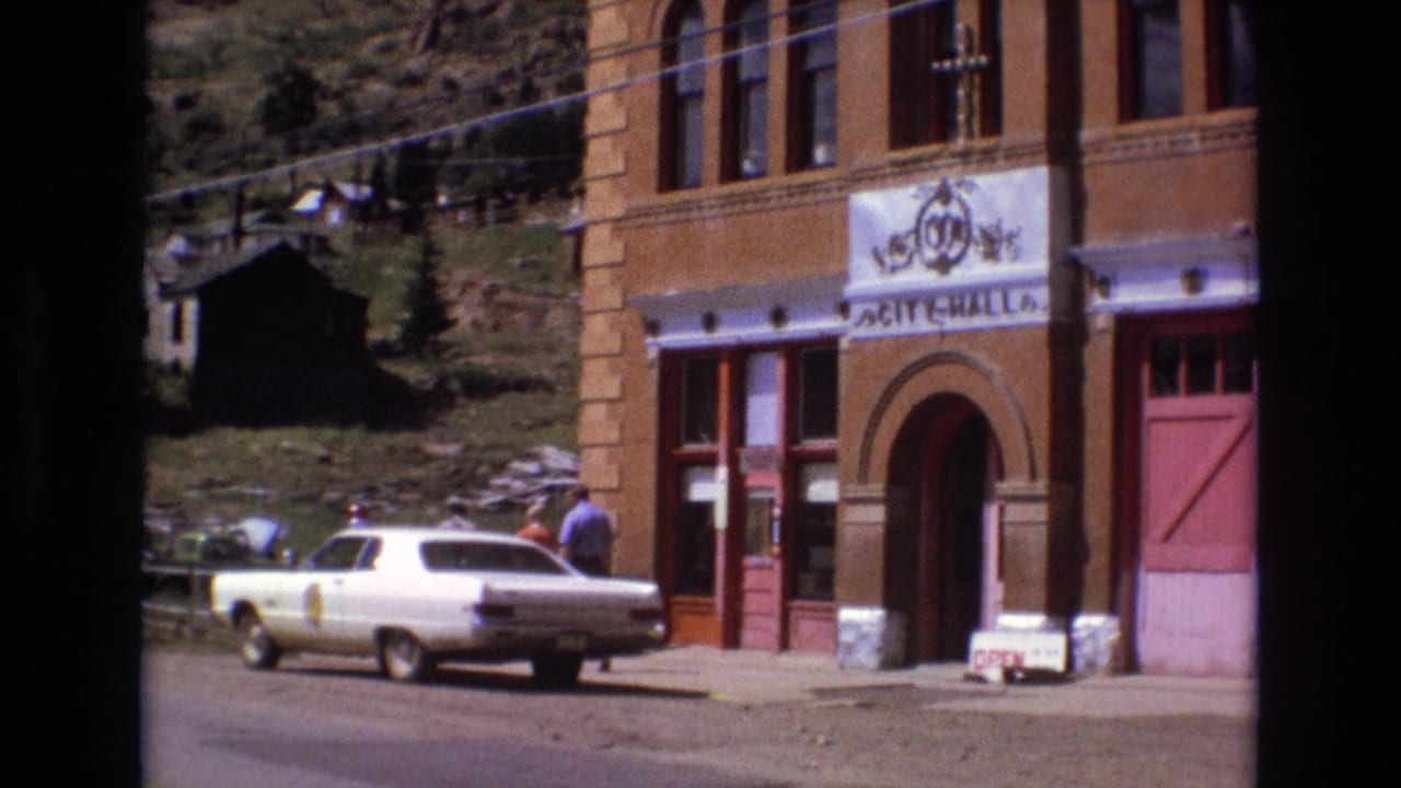White sedan parked in front of City Hall as a man walks near the entrance.