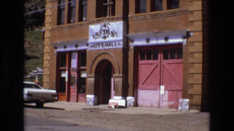 Final 1973 8mm frame holds on the Colorado Springs City Hall entrance, red doors, sidewalk OPEN sign, and a white sedan partly visible at left.