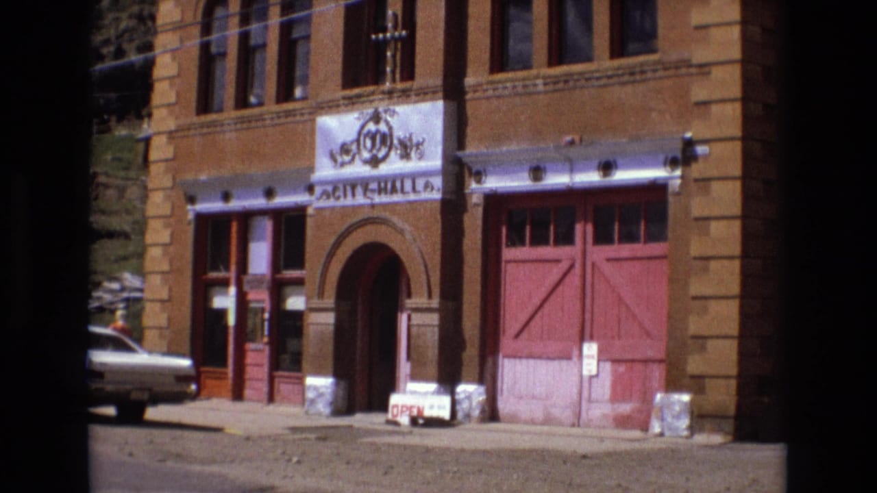 Brick civic building with red garage doors, arched entry, white sedan, and open sidewalk sign.