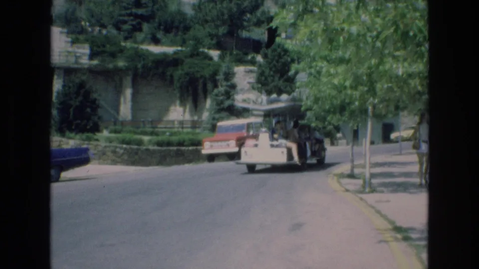 The final frame shows the 1973 Colorado Springs tour vehicle receding along a curved residential street, with leafy branches, curb, sidewalk, and stone retaining wall in view.