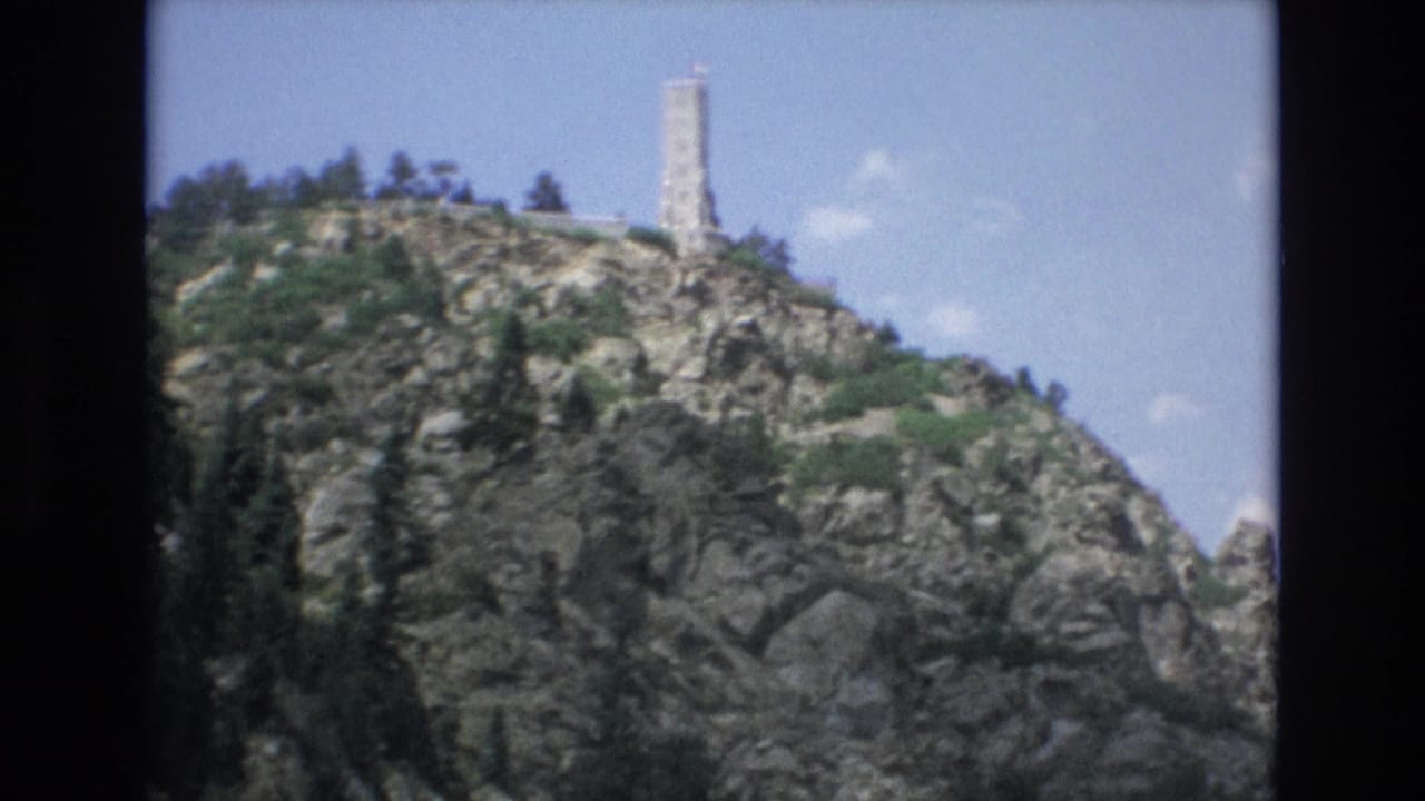 Rocky hilltop with a tall pale tower and scattered trees.