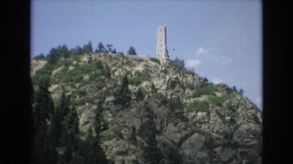1973 Colorado Springs home-movie view of a tall stone tower on a rugged, tree-covered hill, framed by the dark edges of the 8mm scan.