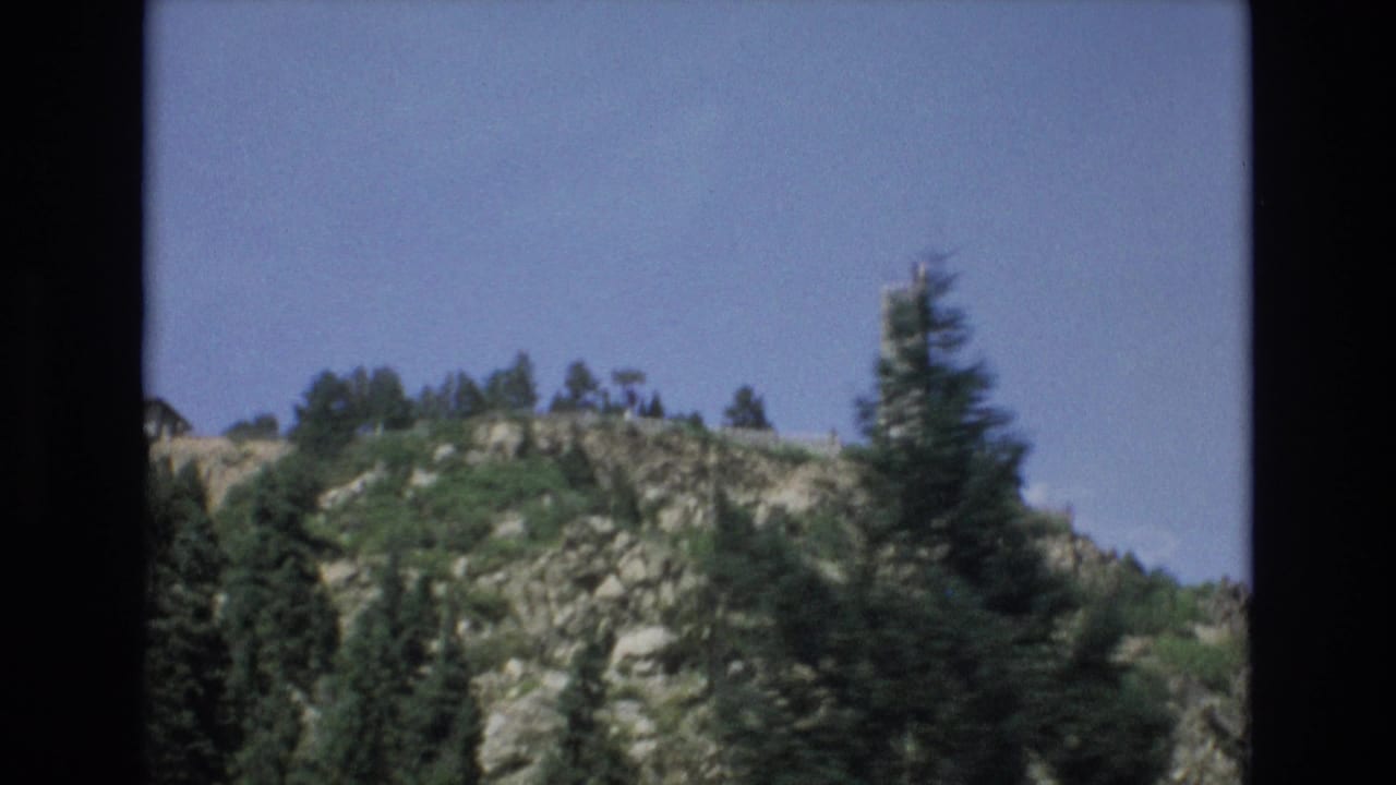 Rocky hillside with evergreens and the tower near the right edge.