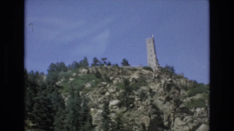 1973 8mm frame from Colorado Springs with a slightly tilted handheld view of the tower above a rocky, wooded hill.
