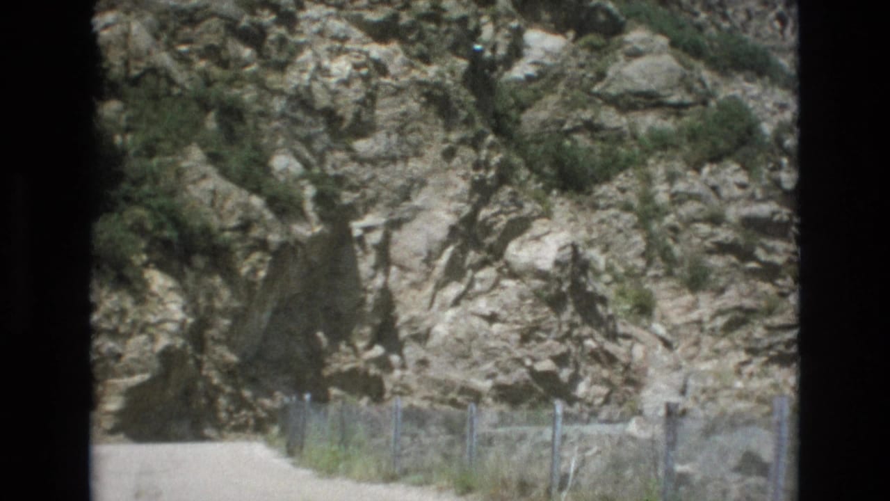 1973 Colorado Springs frame with a fenced dirt route running below a textured rock wall, filmed from a forward-moving home-movie perspective.