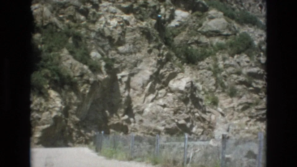 1973 Colorado Springs frame with a fenced dirt route running below a textured rock wall, filmed from a forward-moving home-movie perspective.