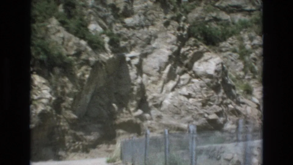 1973 Colorado Springs frame showing a rugged rock formation above a narrow dirt path bordered by low wire fencing and sparse vegetation.