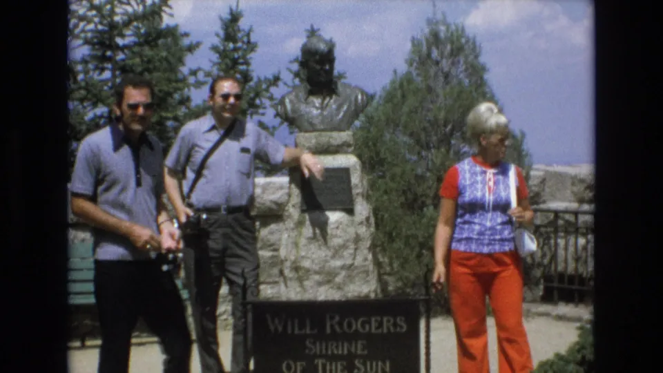At the Will Rogers Shrine of the Sun, tourists stand near a bronze bust and stone plaque while one man carries a camera.
