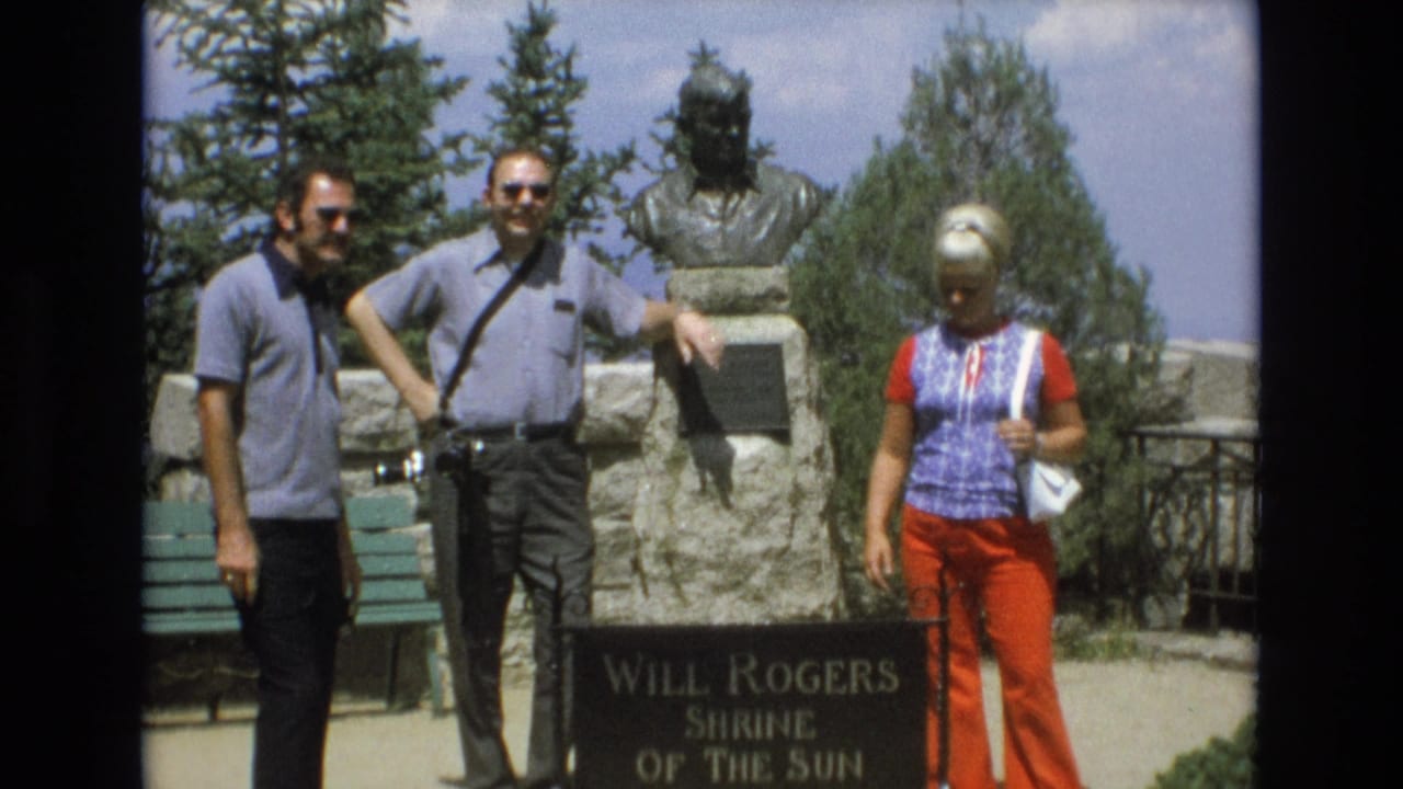 Three adult tourists stand at the Will Rogers Shrine of the Sun in Colorado Springs, with a stone monument, bronze bust, trees, and bright 1970s clothing visible.