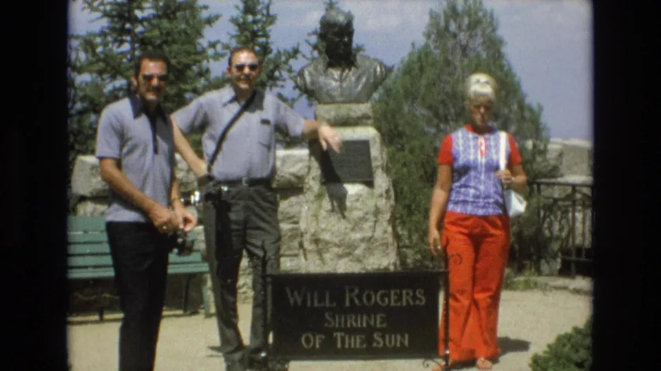 The final frame shows the three adult tourists still posed at the Will Rogers Shrine of the Sun in Colorado Springs, with the sign, bust, and landscaped overlook area visible.