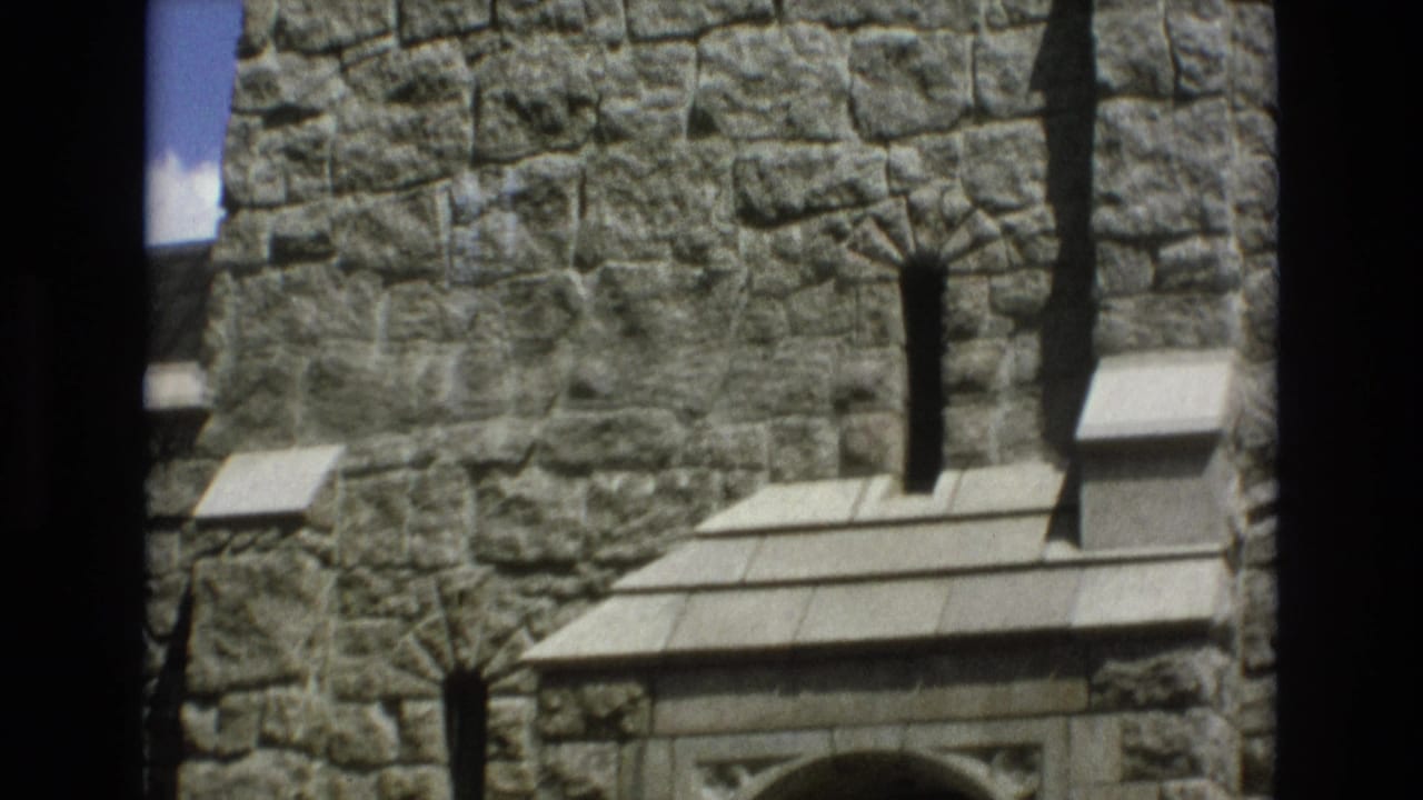 1973 Colorado Springs 8mm frame showing the lower portion of a gray stone tower facade, narrow vertical slit windows, projecting stone ledges, and part of a small arched doorway.