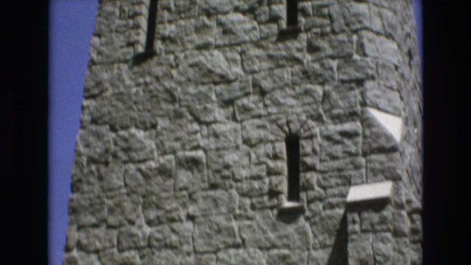 1973 Colorado Springs 8mm frame showing a curved section of the stone tower, centered on a narrow slit window set into rough masonry with ledges and blue sky at the edge.