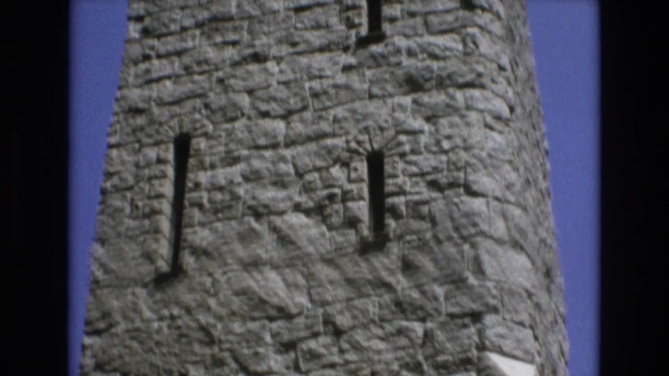 1973 Colorado Springs 8mm frame showing the rounded stone tower facade with two narrow vertical slit windows, rough gray masonry, small ledges, and a clear blue sky edge.