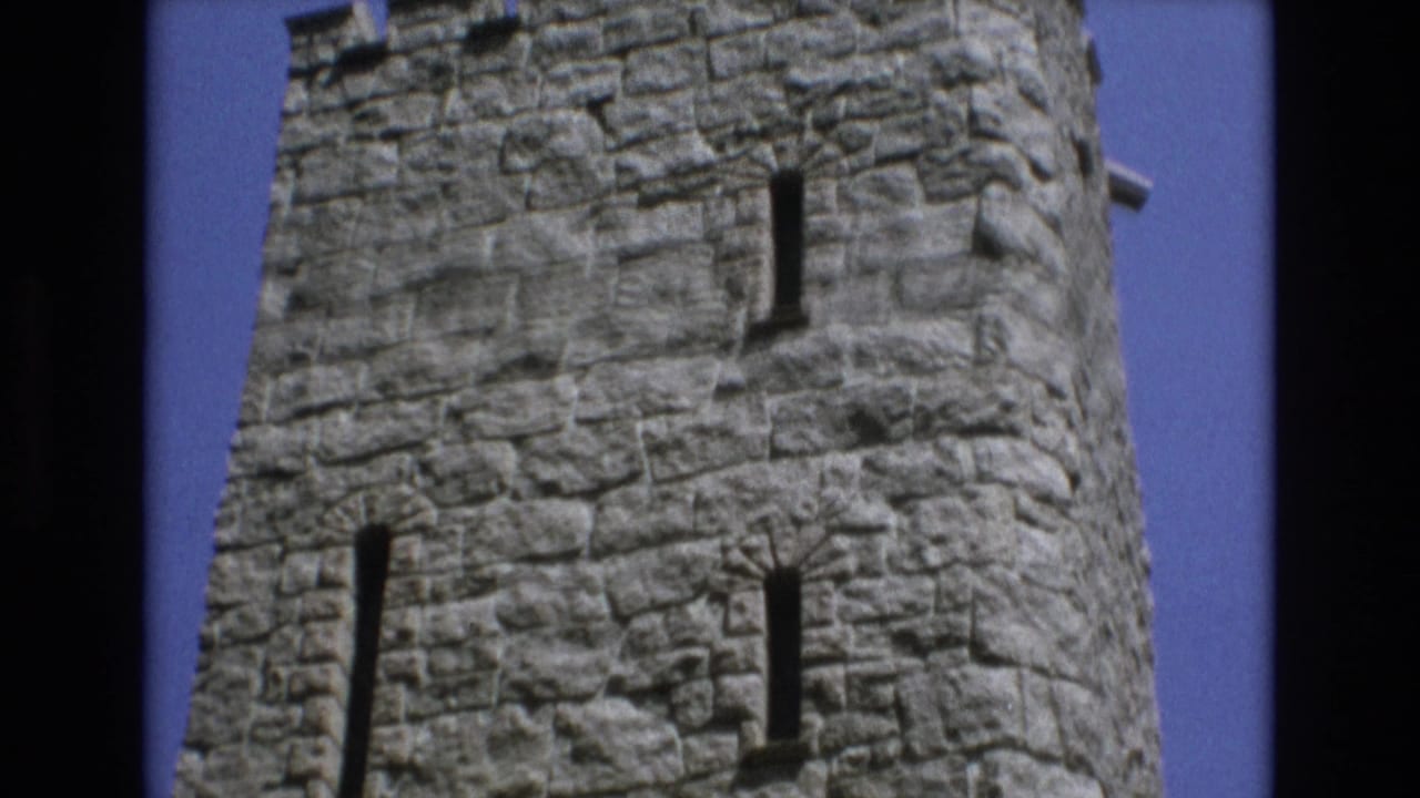 1973 Colorado Springs 8mm frame looking up at a rough stone castle-style tower with narrow vertical windows and crenellated top edges.