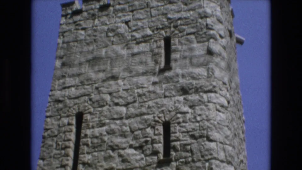 1973 Colorado Springs 8mm frame looking up at a rough stone castle-style tower with narrow vertical windows and crenellated top edges.