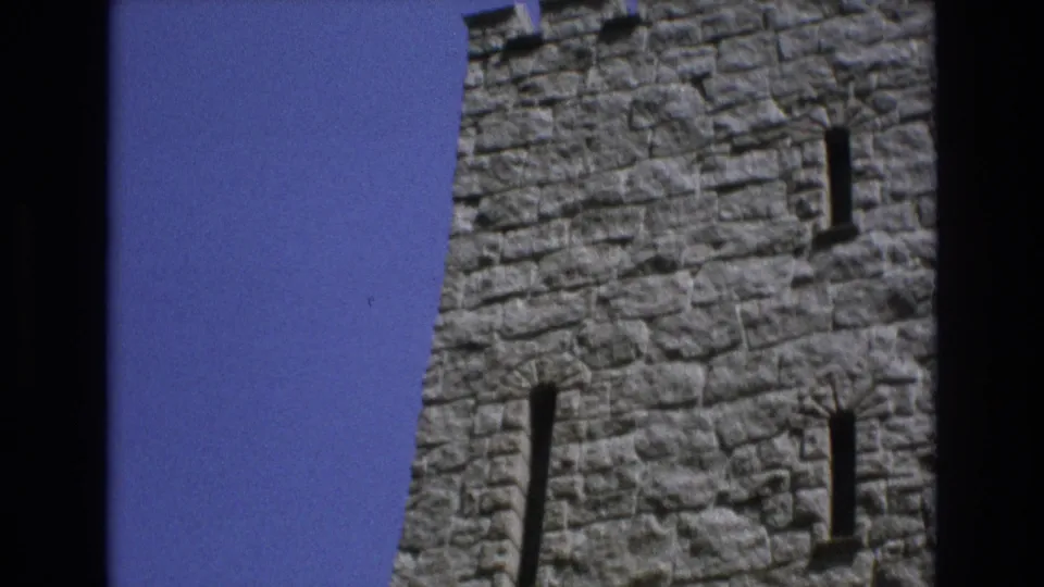 1973 Colorado Springs 8mm frame with a tight upward angle on a castle-style stone tower face, showing stacked masonry and narrow slit windows.