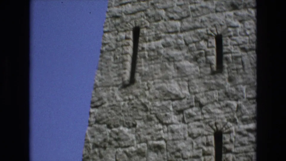 1973 Colorado Springs frame showing a tall section of rough stone castle-style tower with multiple narrow windows and a small amount of sky at the edge.