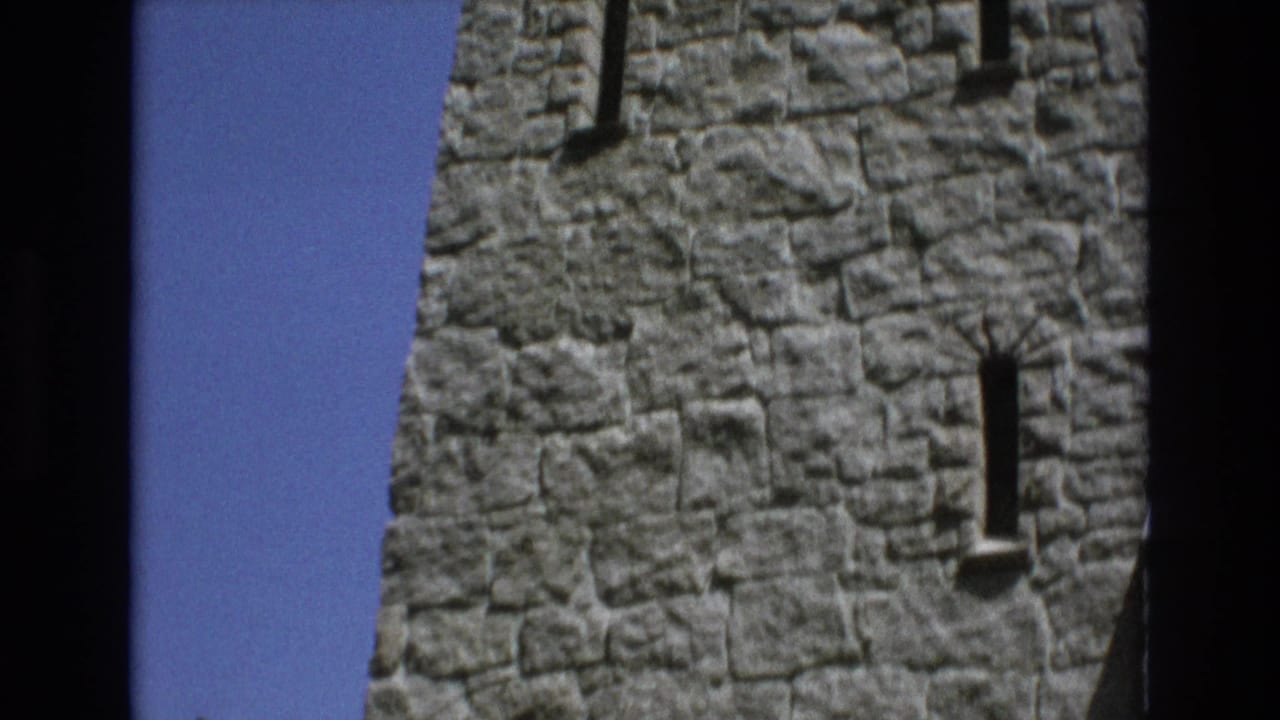 1973 Colorado Springs 8mm frame showing a close visitor-shot view of rough gray stone walls and narrow vertical window openings under a bright blue sky.