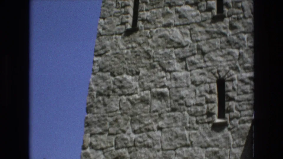 1973 Colorado Springs 8mm frame showing a close visitor-shot view of rough gray stone walls and narrow vertical window openings under a bright blue sky.