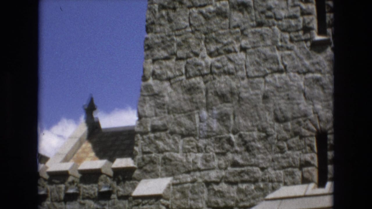 1973 Colorado Springs 8mm frame showing stone wall sections, narrow window openings, battlement-like trim, and part of a small roofline between the masonry.