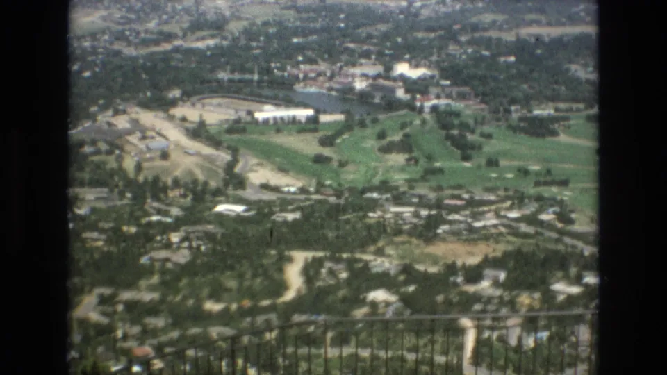 A wide 8mm view from above shows Colorado Springs with green open areas, roads, rooftops, and distant terrain under bright daylight.