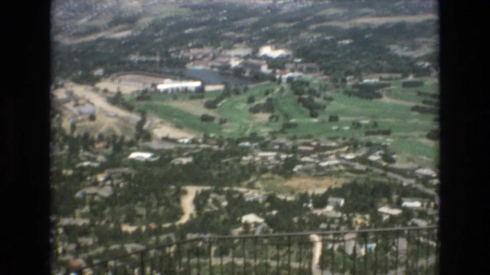 The final frame continues the elevated Colorado Springs panorama, with green grounds, roads, scattered buildings, and distant slopes rendered in soft 8mm color.