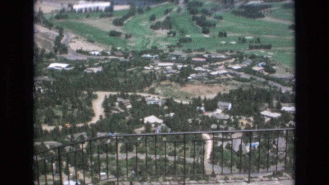 Overlook view across a wooded town and golf course with a metal railing in the foreground.