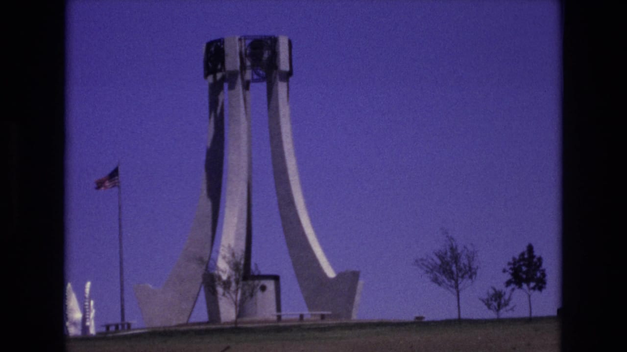 White monument and American flag seen across a lawn under a clear blue sky.