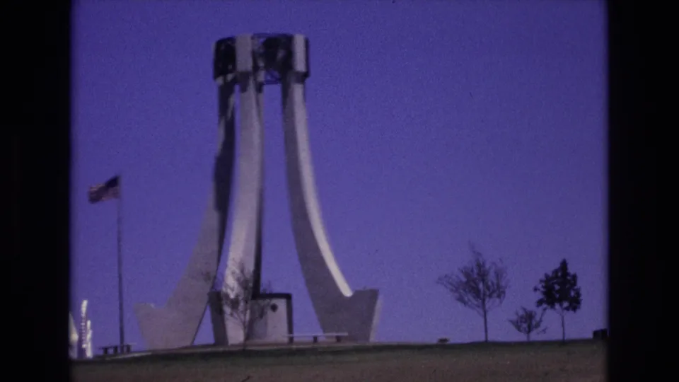1973 Colorado Springs frame of a white public monument on a grassy hill, with an American flag at left, small trees at right, and visible 8mm film texture.