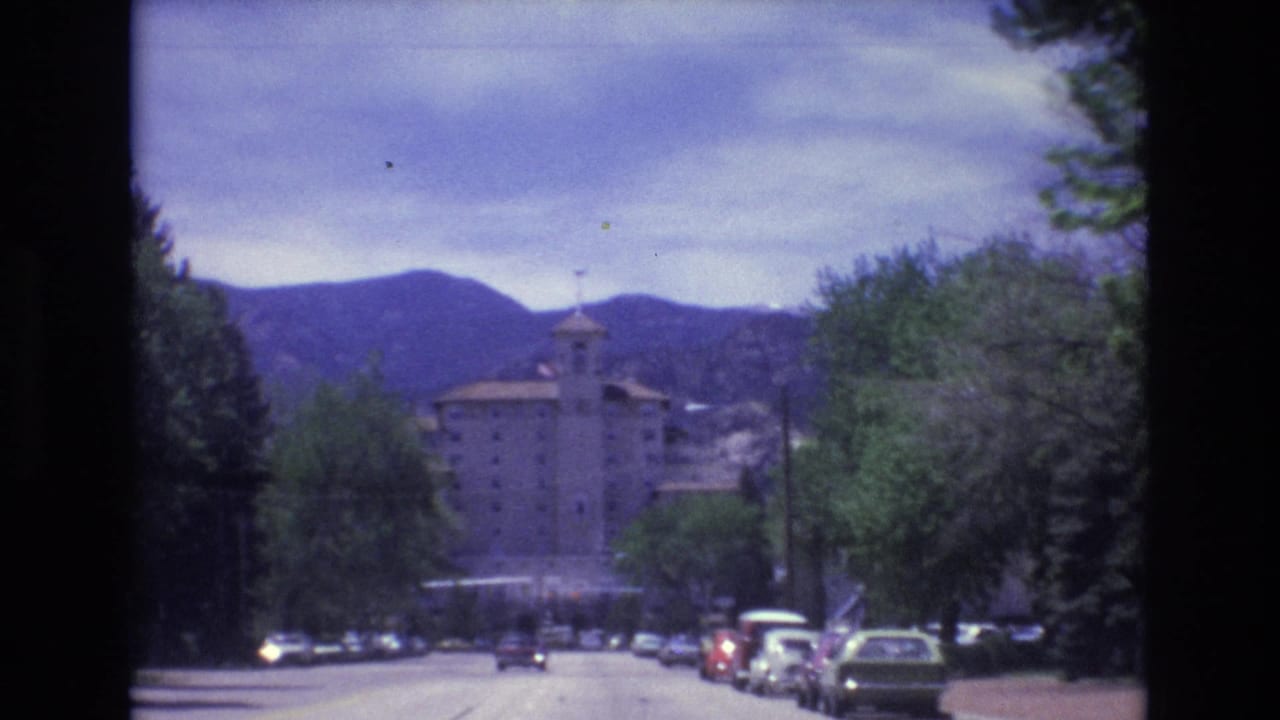 Tree-lined road with cars, a large building, and mountains in the background.