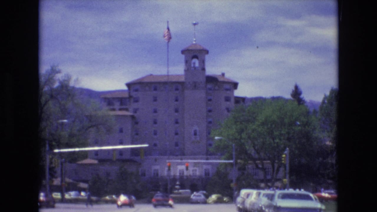 Cars and pedestrians near a red-light intersection in front of a towered building.