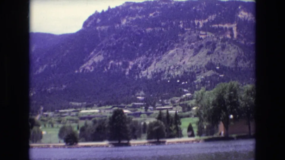 The frame looks across a lake toward trees, small shoreline structures, and a forested mountain in Colorado Springs, based on the supplied clip metadata.