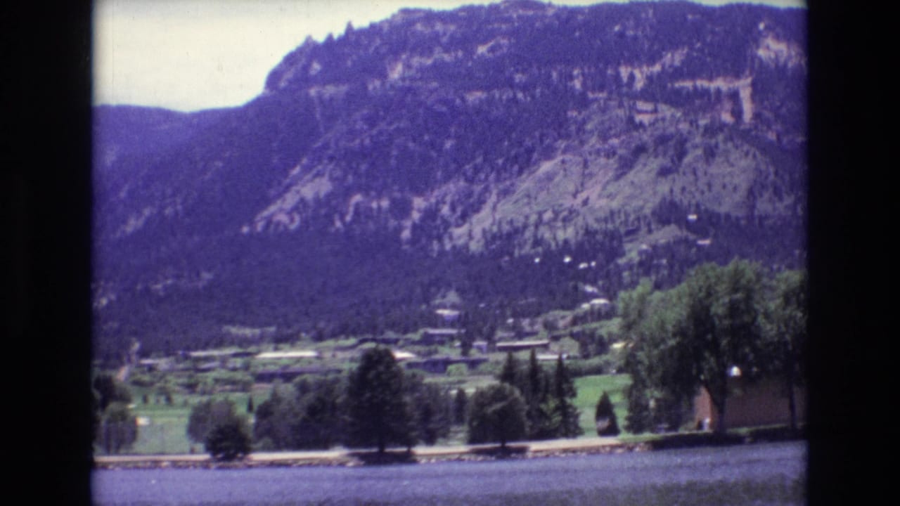 1973 8mm view in Colorado Springs showing water in the foreground, trees and small buildings in a valley, and a forested mountain slope beyond.