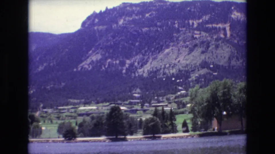 1973 8mm view in Colorado Springs showing water in the foreground, trees and small buildings in a valley, and a forested mountain slope beyond.