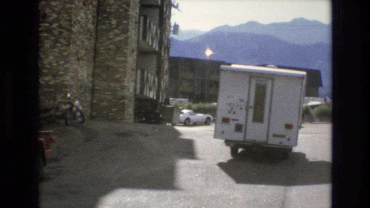 White RV farther down a paved parking area near resort buildings and mountains.
