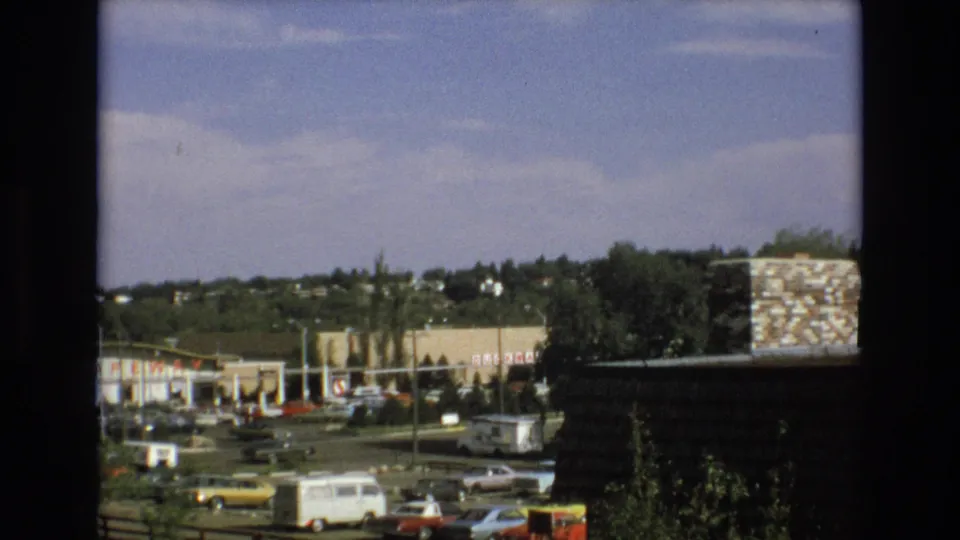 Colorado Springs shopping-center view from 1973 showing parked classic cars, a white van, low retail buildings with Safeway signage, trees, and a dark foreground frame edge.