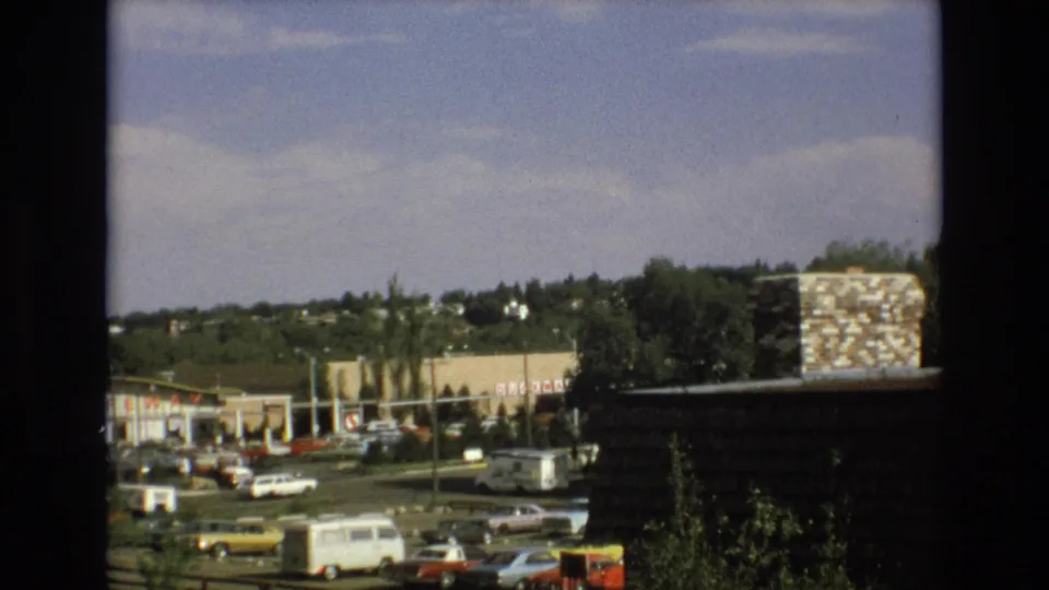 1973 Colorado Springs view of a suburban commercial area with Safeway signage, parked cars, a white van, trees, and a stone chimney in the foreground.