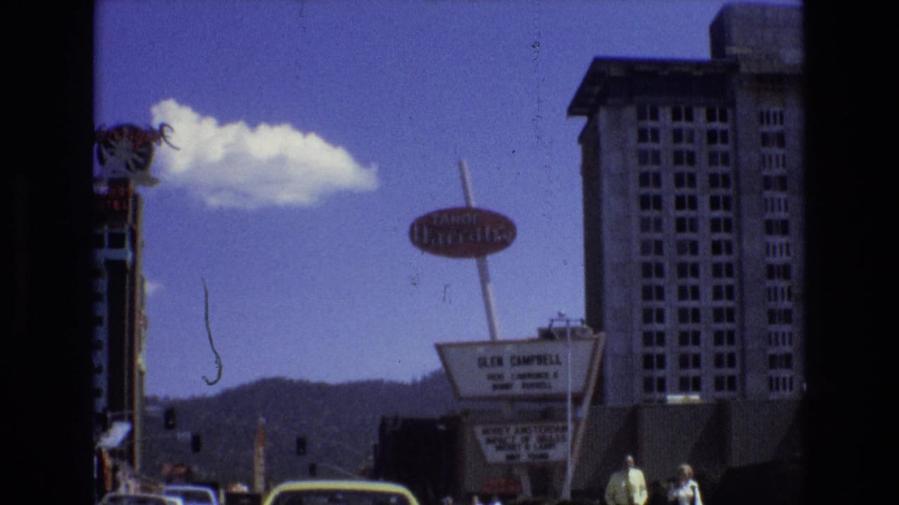 Lake Tahoe, Nevada street frame showing the Tropicana sign, hotel marquee, pedestrians near the sidewalk, cars in traffic, distant mountains, and a tall building.