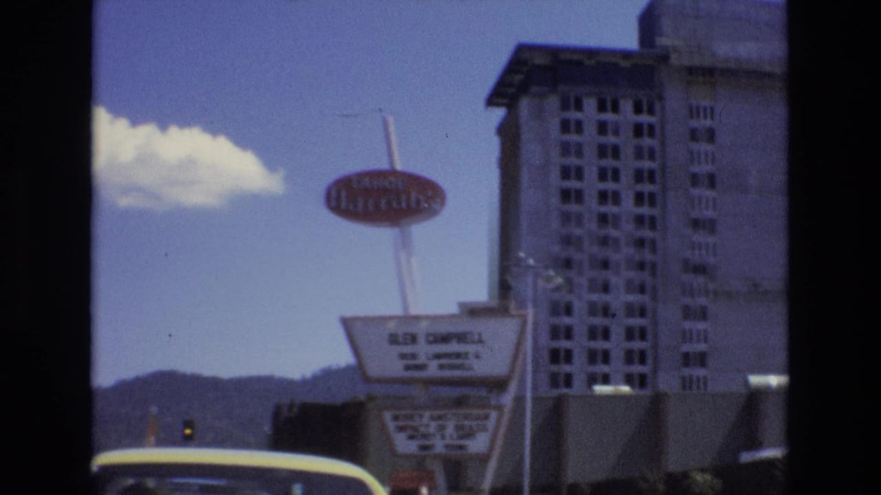 1973 Lake Tahoe, Nevada home-movie frame showing the red Tahoe Harrah's sign, tall hotel tower, roadside marquee, distant hills, and a yellow car roof in the foreground.