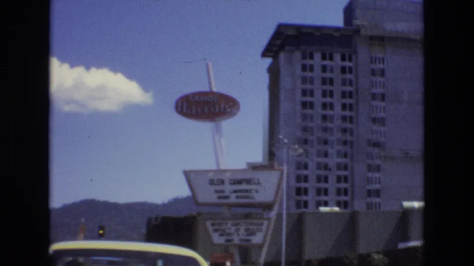 1973 Lake Tahoe, Nevada home-movie frame showing the red Tahoe Harrah's sign, tall hotel tower, roadside marquee, distant hills, and a yellow car roof in the foreground.